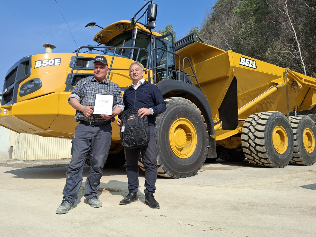 Pracownik Kopalni Wapienia "Czatkowice" sp. z o.o. w czapce z daszkiem z dyplomem ukończenia kursu kierowania wozidłem Bell B50e z przedstawicielem firmy Kiesel Poland. W tle wozidło Bell B50e